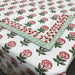 A white cotton tablecloth with a red and green floral block print pattern and a matching folded corner showing a red and green geometric border.