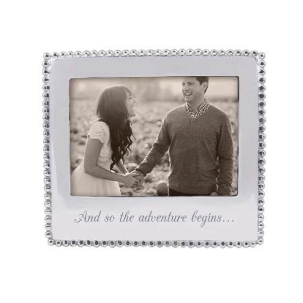 Decorative photo frame with a couple holding hands and text 'And so the adventure begins...' on a white background.