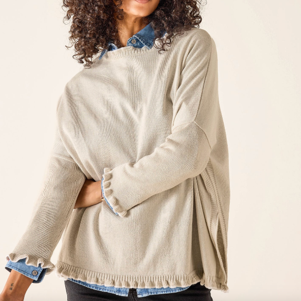Woman wearing a beige sweater with denim trim on a plain background