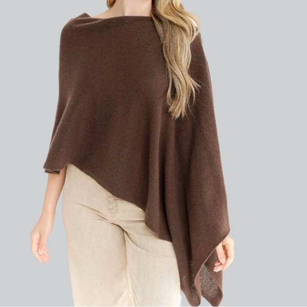 A woman wearing a brown knit poncho-style top with beige pants, shown against a plain gray background.