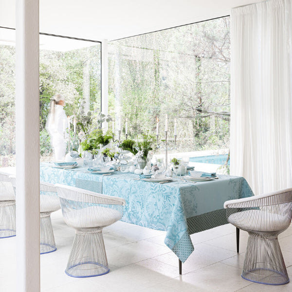 Dining room with a table set for a meal, surrounded by large windows with a view of greenery.