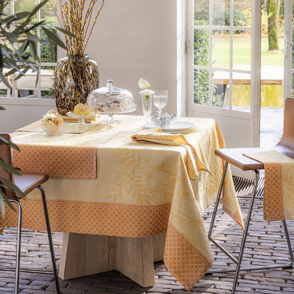 Dining table set with a decorative tablecloth in a bright room with large windows.