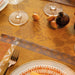An autumn-themed table setting featuring a warm mustard yellow tablecloth with a leaf pattern, matching placemats, a silver fork, a striped plate, and decorative fruit.