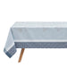 A light blue tablecloth with a subtle floral pattern and a darker blue geometric border, draped over a table with a wooden leg visible against a white background.