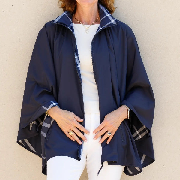 A woman wearing a navy blue poncho-style raincoat with a plaid pattern lining, standing against a plain beige wall.