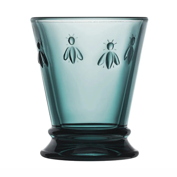 A translucent smoky blue-green glass tumbler with embossed bee motifs on the front, set against a plain white background.