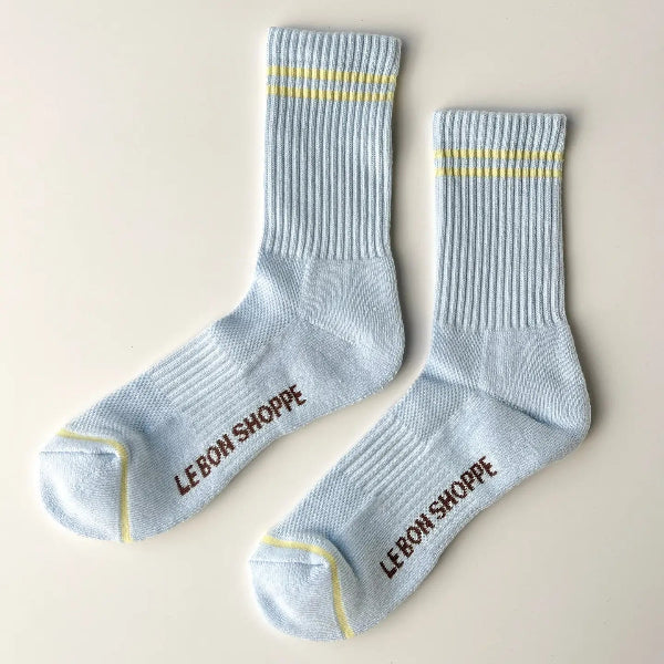 Pair of light blue socks with yellow accents and 'Lebon Shoppe' branding on a beige background