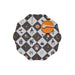 A scalloped circular placemat with a Halloween-themed harlequin pattern of black and white checkers, featuring illustrations of pumpkins, witches, bats, and houses. It has a solid orange center with a white spoon resting on top, set against a plain white background.