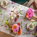 Table setting with floral tablecloth, teacups, and small floral arrangements.