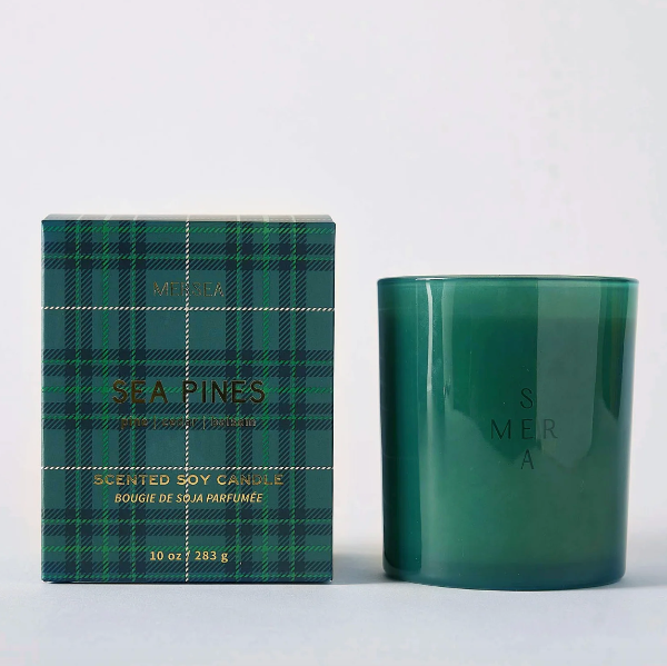A green glass scented soy candle next to its matching green plaid packaging box, featuring the brand name MESA and scent name SEA PINES.