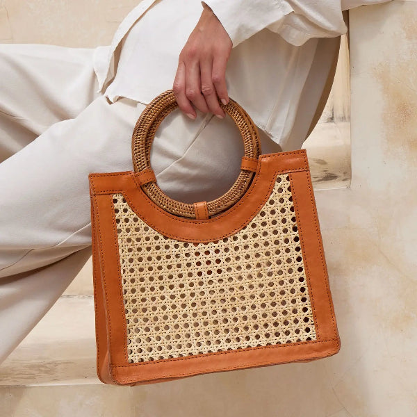 Brown woven handbag held by a person wearing a white outfit on a light background