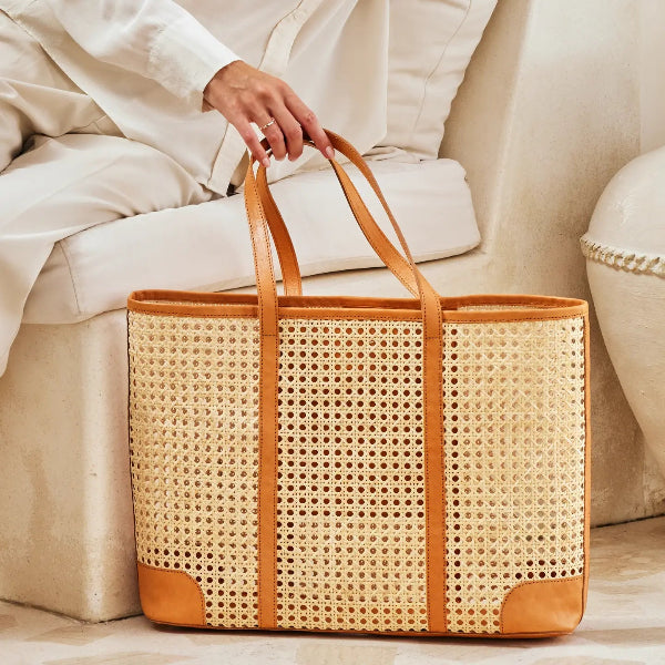 Person holding a woven basket with brown handles on a light-colored couch.