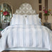 Striped bedding set on a bed with decorative pillows and flowers in the room.