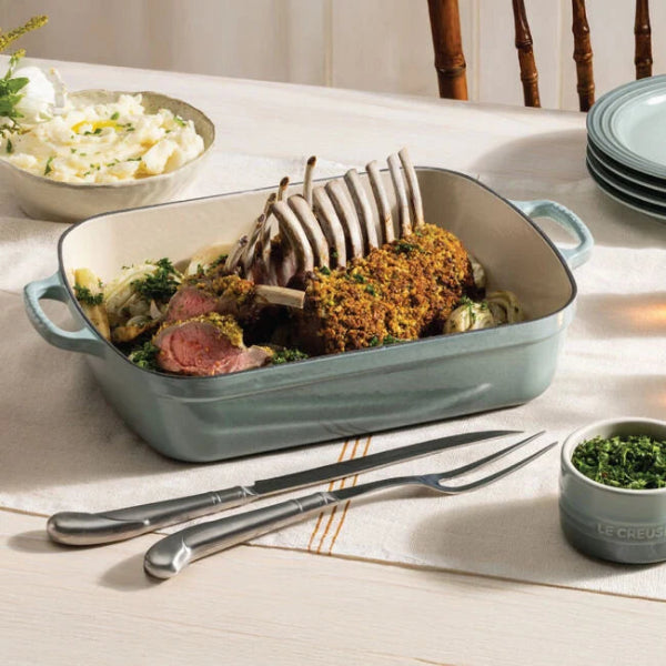 baking dish with roasted meat and vegetables on a table with cutlery and side dishes.
