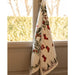 A cream-colored kitchen towel with a Christmas print featuring red stockings, pine branches, and a reindeer, hanging from a window.