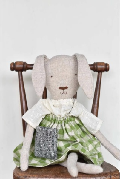 Stuffed rabbit toy with a green dress sitting on a wooden chair against a white background