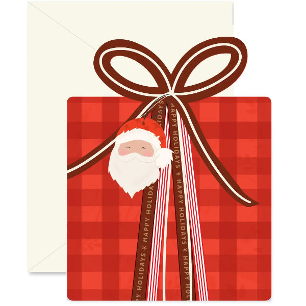 A Christmas greeting card or gift-themed print featuring a red plaid gift box with a large brown ribbon bow, a Santa face charm, and striped ribbons reading 'MERRY HOLIDAYS' and 'SAVOR THE SEASON.' An off-white envelope is visible behind the card on a white background.