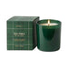 A green glass scented soy candle next to its matching green plaid box, labeled 'MERSEA SEA PINES'. The candle is lit with a visible flame, set against a plain white background.