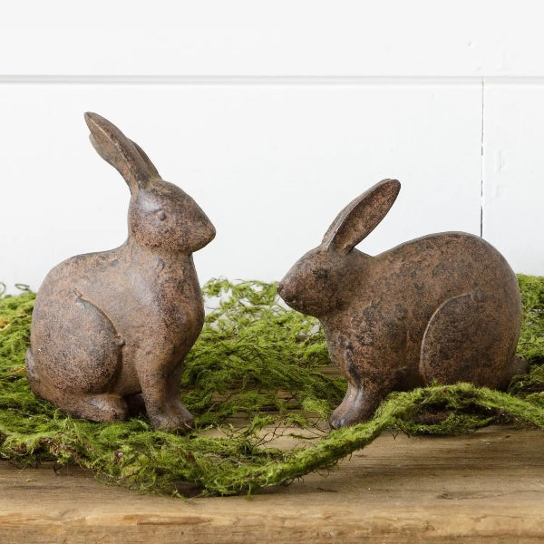 Two rustic rabbit statues on a bed of moss with a white background