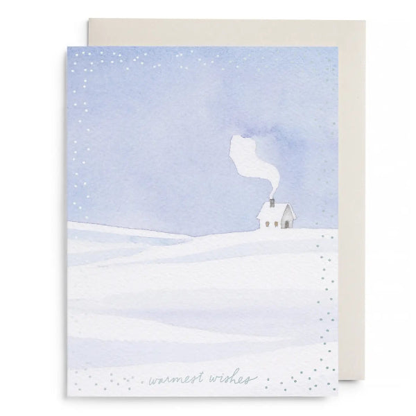 A watercolor-style greeting card showing a snowy landscape with a small house and smoke, placed in front of a plain cream envelope on a white background.