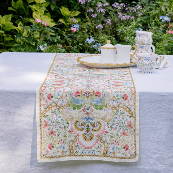 Decorative table runner with floral and bird pattern on a table outdoors.
