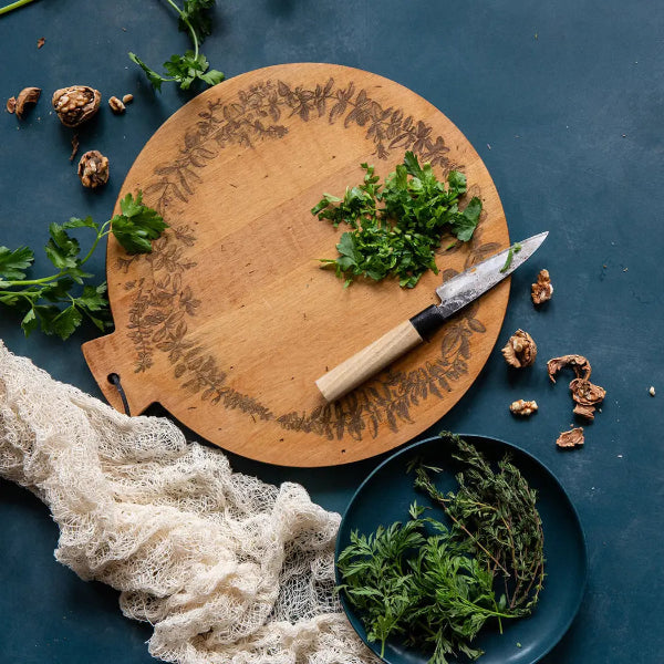 Wooden cutting board with herbs and a knife on a dark surface