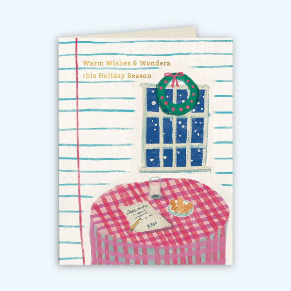 A holiday greeting card featuring an illustrated winter table scene with a pink gingham tablecloth, a green wreath, a window with snow outside, and the text 'Warm Wishes & Wonders this Holiday Season' on a cream striped background.