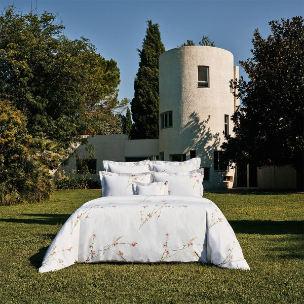 Floral-patterned bedspread on a bed outdoors with a modern building and trees in the background