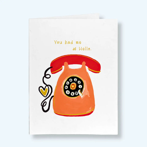 A white greeting card featuring a retro orange rotary telephone illustration with a red receiver and the text 'You had me at Hello.' in yellow, shown against a pale blue background.